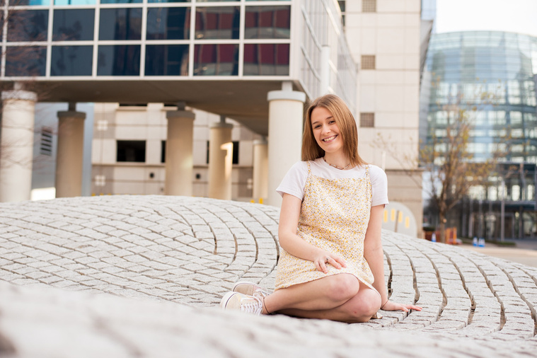 high school senior girl sits on a stone structure with the Devon tower in downtown Oklahoma City behind her
