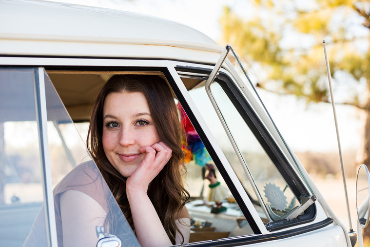 high school senior girl with brown hair wearing a t-shirt and bell bottoms sits and looks out of the open passenger window of a VW bus in a yard in Tuttle Oklahoma