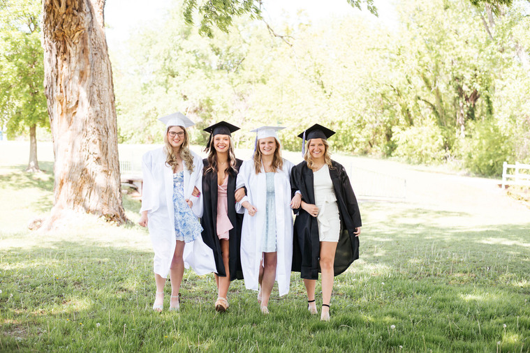 group photo of 4 high school senior girls wearing dresses and caps and gowns walking together arm in arm in a park in Newcastle, Oklahoma