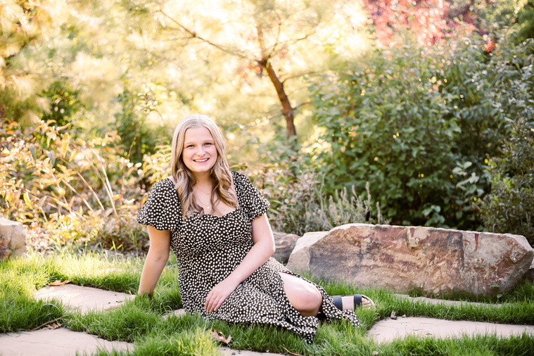 blond high school senior girl wearing a dress sitting in the grass in front of trees and plants at Myriad Gardens in downtown Oklahoma City