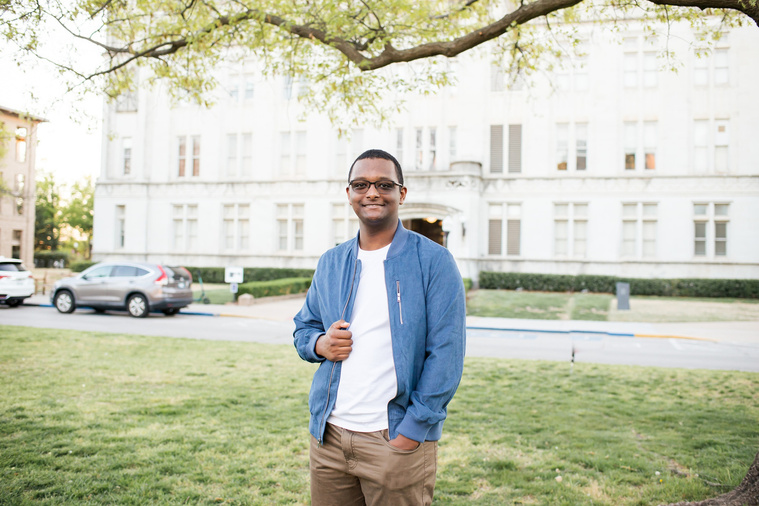 portrait of an african-american high school senior boy wearing a blue jacket and khakis standing and smiling in the middle of the Parrington Oval on the OU campus in Norman Oklahoma