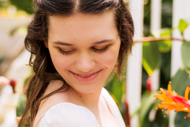 close up photo of a high school senior girl with long brown hair wearing a white blouse smiling down her shoulder inside the Crystal Bridge at Myriad Gardens in Oklahoma City 