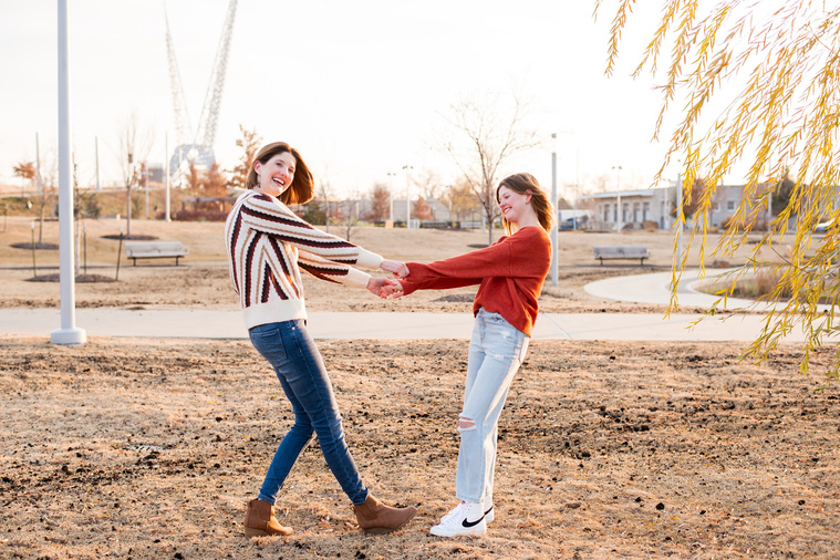 a mom and her teen daughter hold hands and twirl together laughing Scissortail Park in Oklahoma City