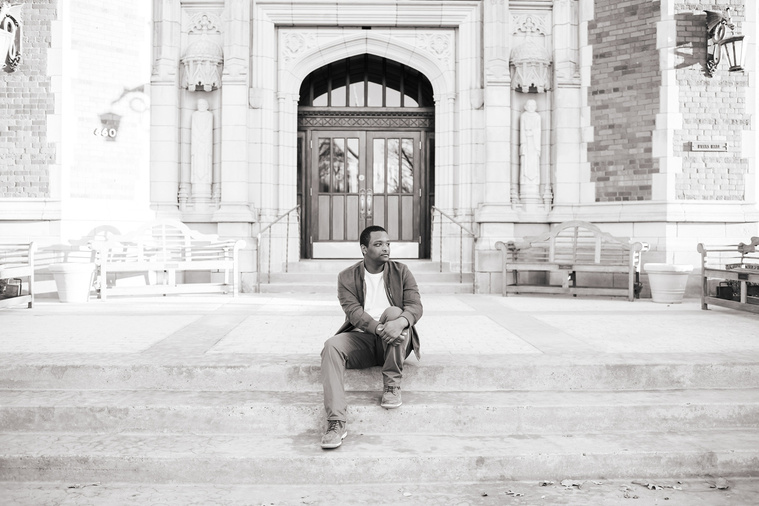 black and white portrait of an african-american high school senior boy sitting on the front steps of Evans Hall on the OU campus in Norman Oklahoma