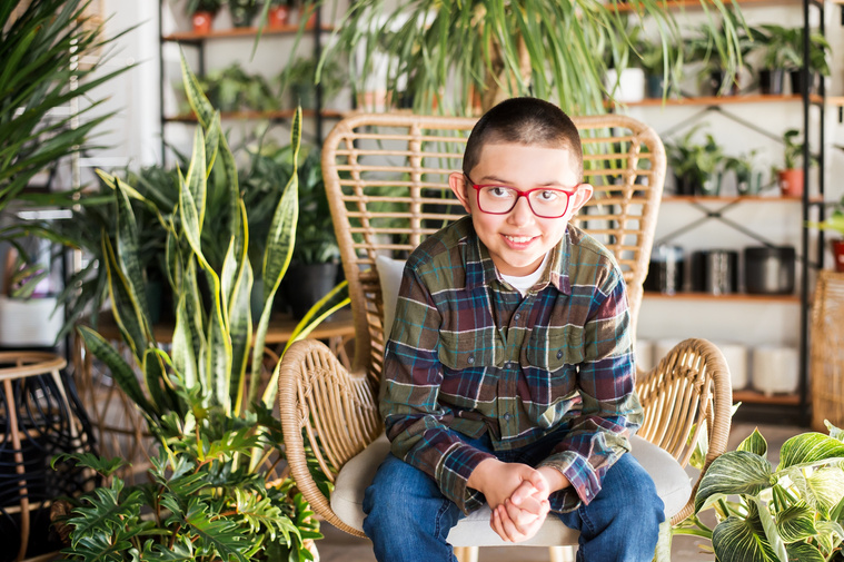 a young boy sits in a wicker chair and smiles at a plant shop in Oklahoma City Oklahoma