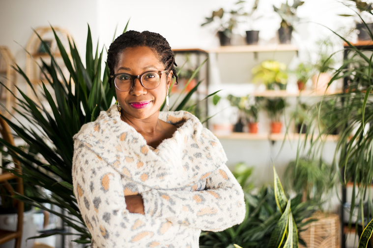  a professional woman stands with arms crossed and smiles in front of plants at a plant shop in Oklahoma City Oklahoma