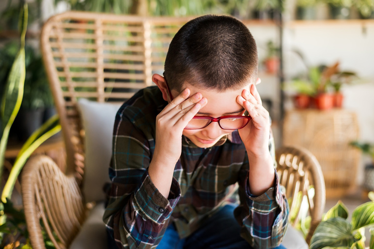 a young boy is sitting and thinking hard with his hands on his temples as he sits in a wicker chair at a plant shop in Oklahoma City Oklahoma