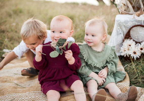 3 young children sit together on a rug in a field in Oklahoma smiling and playing