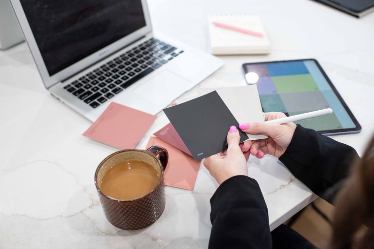 still shot of a graphic designer's hands holding color swatches with her laptop and tools around her and a cup of coffee at a branding photo session