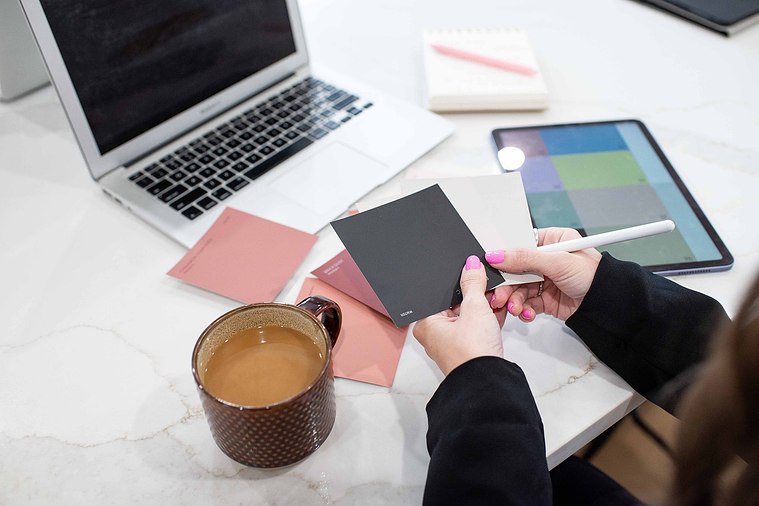 still shot of a graphic designer's hands holding color swatches with her laptop and tools around her and a cup of coffee at a branding photo session
