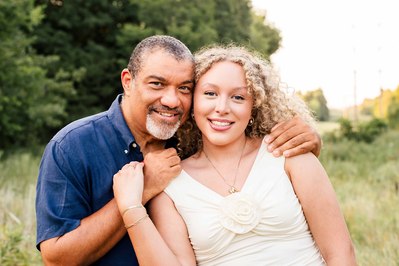 a dad hugs his teen daughter close and smiles with her in front of an open field in the country in Norman Ok.