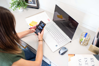 personal brand photo session of a female relator looking over her shoulder down at her desk with a laptop, planner, personal photos and working on her phone in Newcastle, Oklahoma