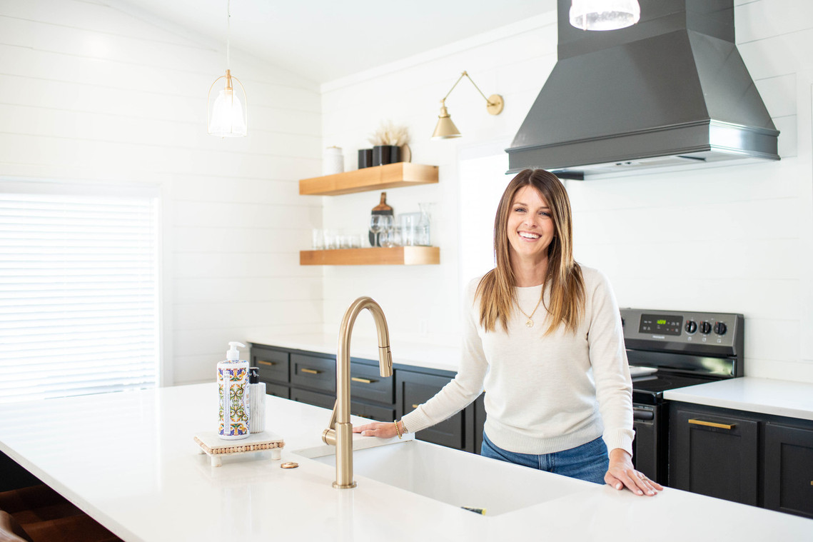 lifestyle headshot of a pretty woman realtor standing in an empty kitchen smiling at camera like she is about to show the space to a client