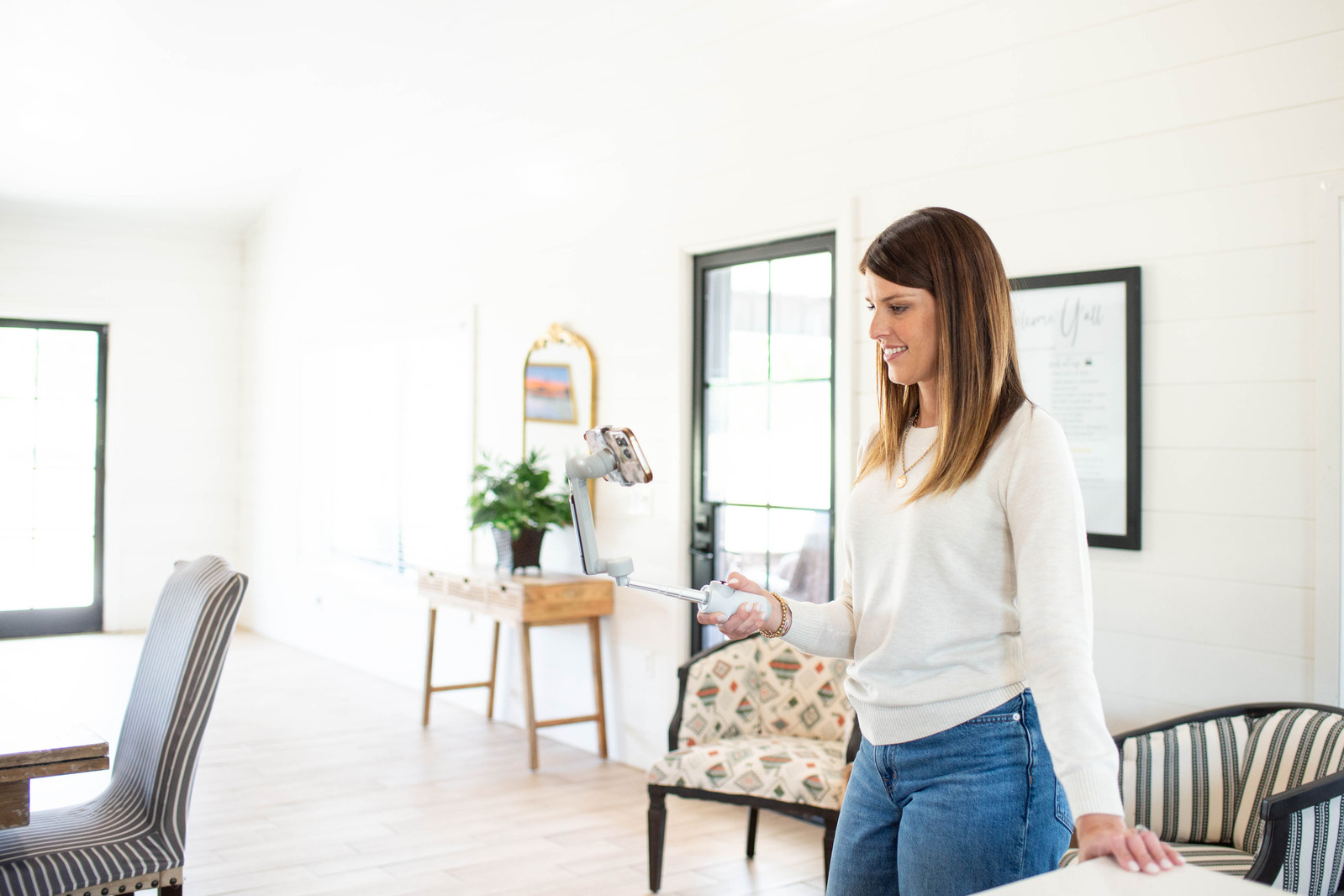 an attractive young woman real estate agent holds a gimbal with a phone to give a virtual tour of a living room in a home for sale taken as a brand photo for her business