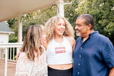 parents hug together and look at their college freshman daughter in front of their wraparound porch at their home in Norman Oklahoma