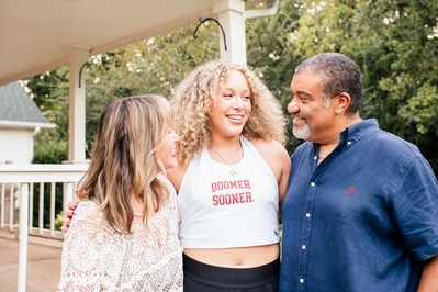 parents hug together and look at their college freshman daughter in front of their wraparound porch at their home in Norman Oklahoma