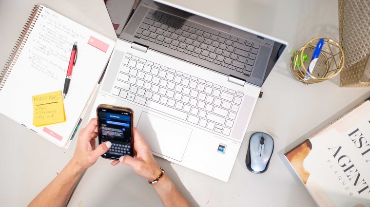 overhead shot of a working realtor holding her phone texting a client with her laptop, planner and office supplies around her at a branding photoshoot in Oklahoma.
