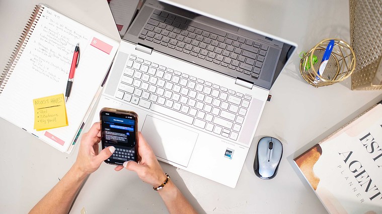 overhead shot of a working realtor holding her phone texting a client with her laptop, planner and office supplies around her at a branding photoshoot in Oklahoma.