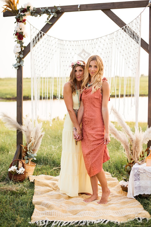 A mom and teen daughter dressed in boho style pose in front of boho decorations and a field and pond in the country in Oklahoma