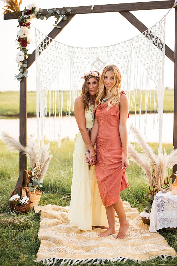 A mom and teen daughter dressed in boho style pose in front of boho decorations and a field and pond in the country in Oklahoma