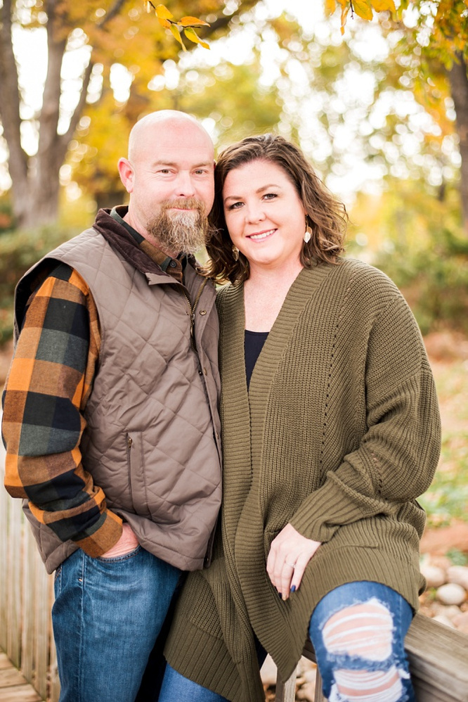 A husband and wife hug together on a wooden footbridge with fall color around them at Will Rogers Gardens in Oklahoma City, Oklahoma
