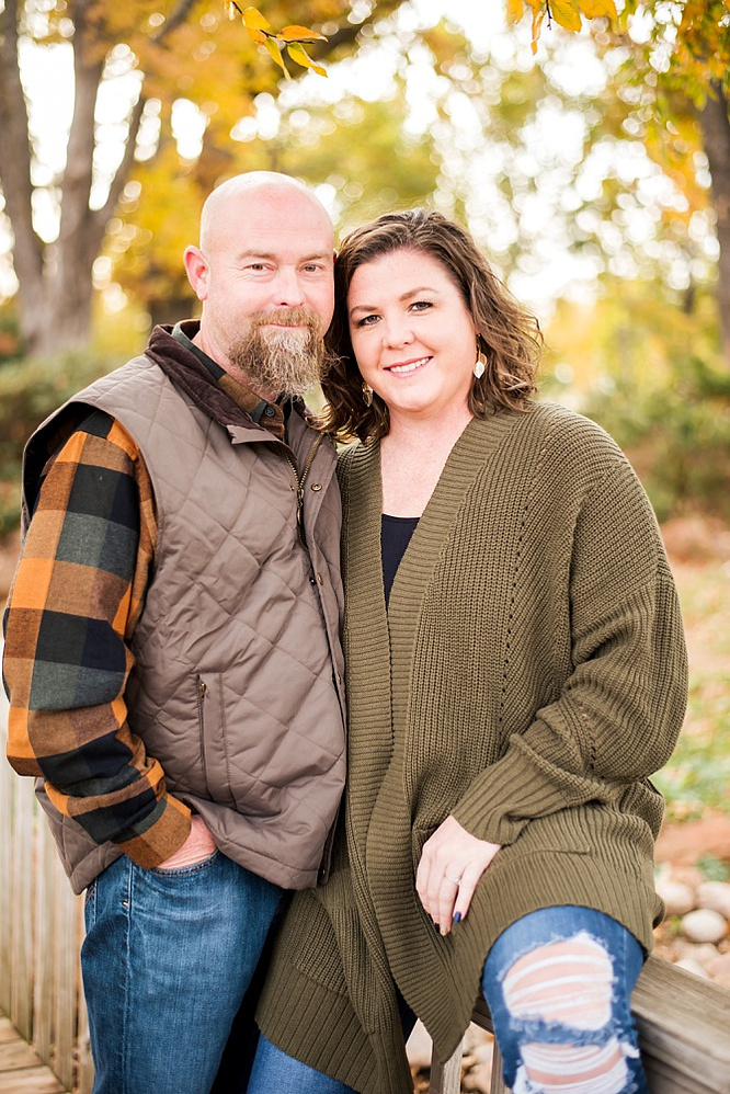 A husband and wife hug together on a wooden footbridge with fall color around them at Will Rogers Gardens in Oklahoma City, Oklahoma