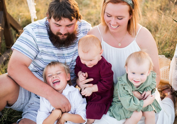 A family with three young children hug and laugh in a field in Tuttle, Oklahoma