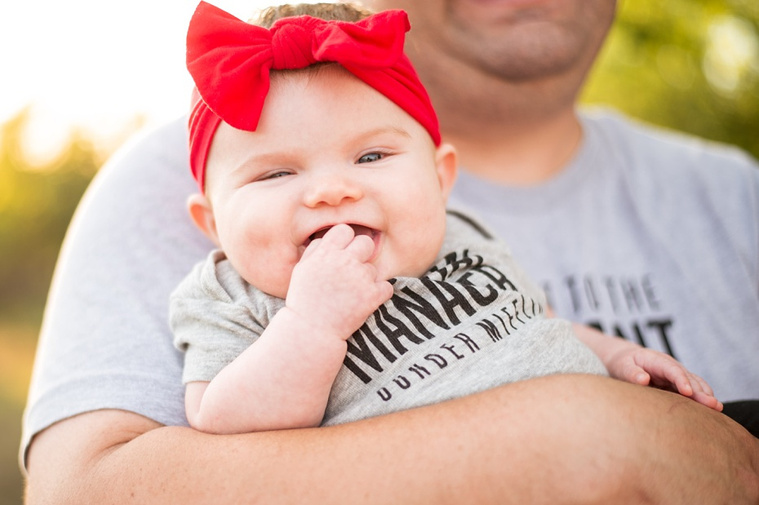 An adorable baby girl in her dad's arms smiles big at the camera.