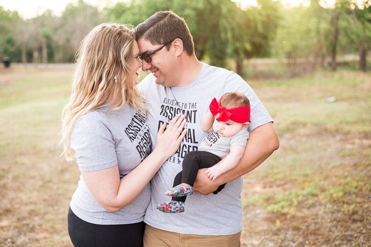 Mom and Dad hold their baby girl in the park wearing 