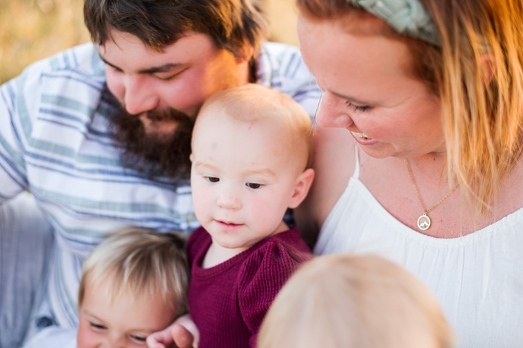 A family with three young children hug and laugh in a field at a family photo session in Tuttle, Oklahoma