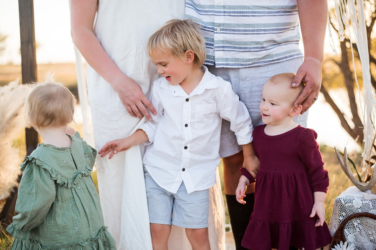Three young children stand in front of their parents interacting with each other in a field at a family photo session in Tuttle, Oklahoma