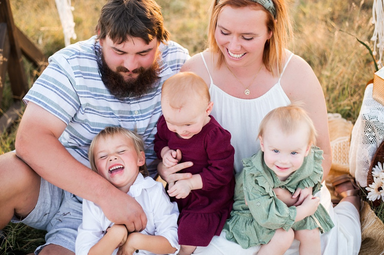 A family with three young children hug and laugh in a field in Tuttle, Oklahoma