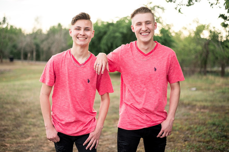 Two teen brothers dressed alike in red shirts and black jeans stand near each other in a park in Tuttle Oklahoma