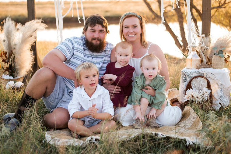 A family with three young children hug and laugh in a field at a family photo session in Tuttle, Oklahoma