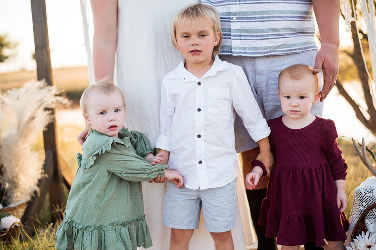 Three young children hold hands in front of their parents in a field at a family photo session in Tuttle, Oklahoma
