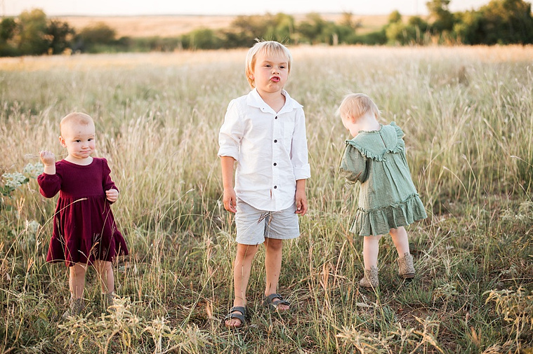Three young children stand and play in a field at a family photo session in Tuttle, Oklahoma