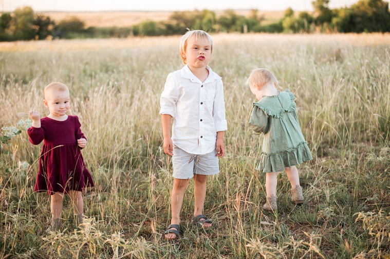 Three young children stand and play in a field at a family photo session in Tuttle, Oklahoma