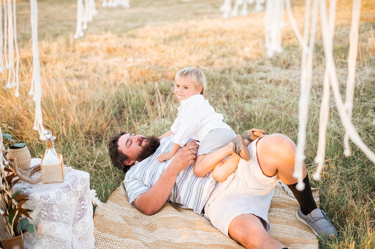 a father lays on his back with his son on his stomach playing in a field at a family photo session in Tuttle, Oklahoma