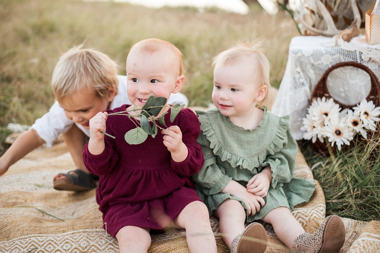 Three young children hold sit on a tan rug playing in a field at a family photo session in Tuttle, Oklahoma