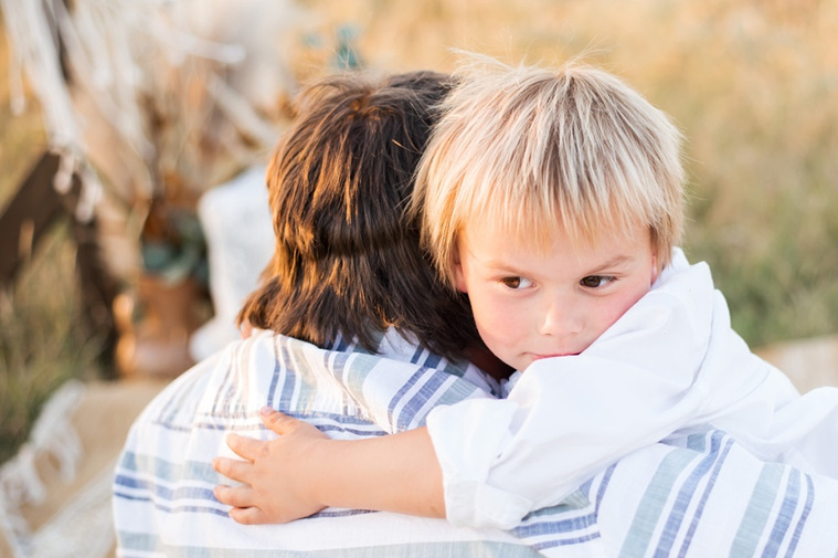 A young boy facing camera holds on to his dad's neck and feels secure in a field at a family photo session in Tuttle, Oklahoma
