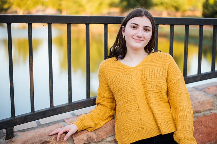A high school senior girl stands on a stone bridge in front of a pond at Shannon Springs Park in Chickasha, Oklahoma 