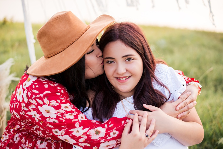 A mom and teen daughter dressed in boho style pose in front of boho decorations and a field and pond in the country in Oklahoma