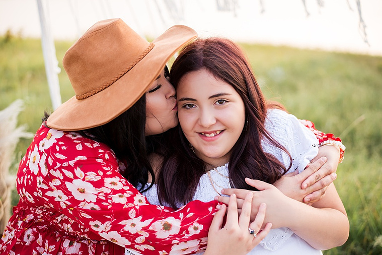 A mom and teen daughter dressed in boho style pose in front of boho decorations and a field and pond in the country in Oklahoma