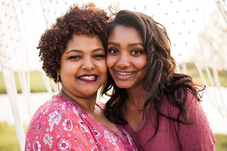 A mom and teen daughter dressed in boho style pose in front of boho decorations and a field and pond in the country in Oklahoma