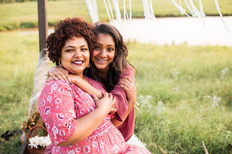 A mom and teen daughter dressed in boho style pose in front of boho decorations and a field and pond in the country in Oklahoma