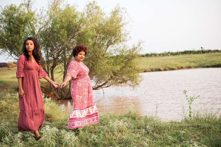 A mom and teen daughter dressed in boho style pose walk in a field near a pond in the country in Oklahoma