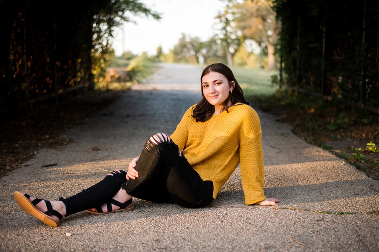 A high school senior girl sits on a path in front of an ivy covered structure in Shannon Springs Park in Chickasha, Oklahoma 