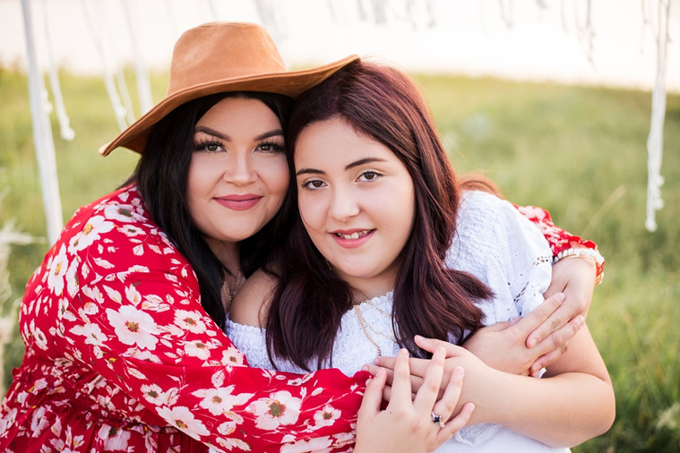 A mom and teen daughter dressed in boho style pose in front of boho decorations and a field and pond in the country in Oklahoma