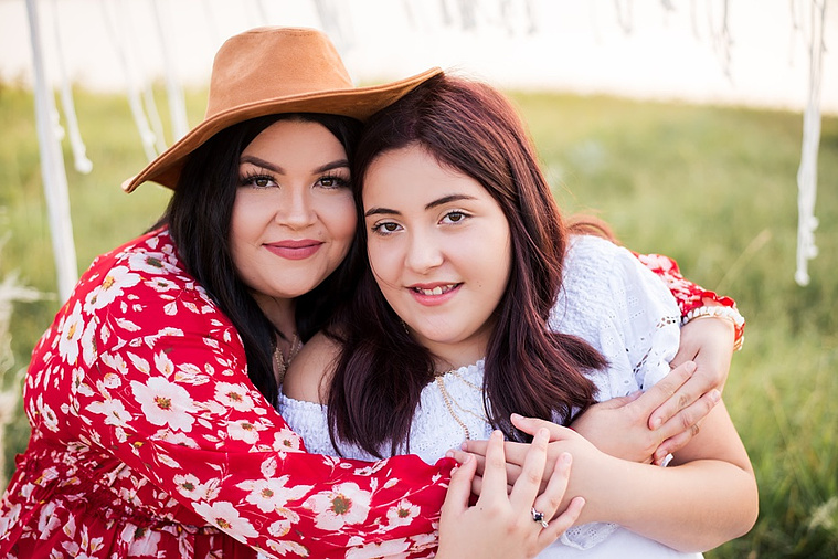 A mom and teen daughter dressed in boho style pose in front of boho decorations and a field and pond in the country in Oklahoma