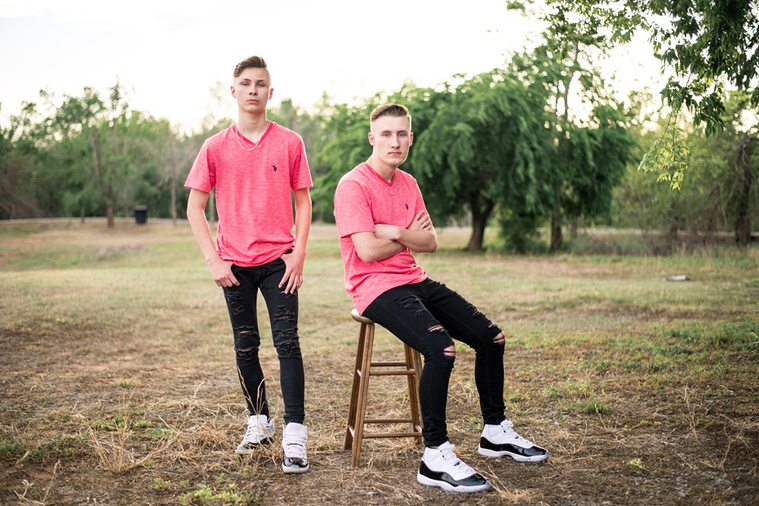 Two teen brothers dressed alike in red shirts and black jeans stand near each other in a park in Tuttle Oklahoma